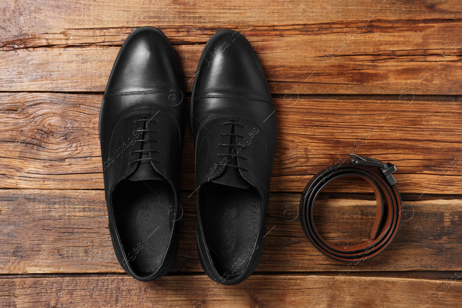 Photo of Pair of black leather men shoes and belt on wooden background, flat lay