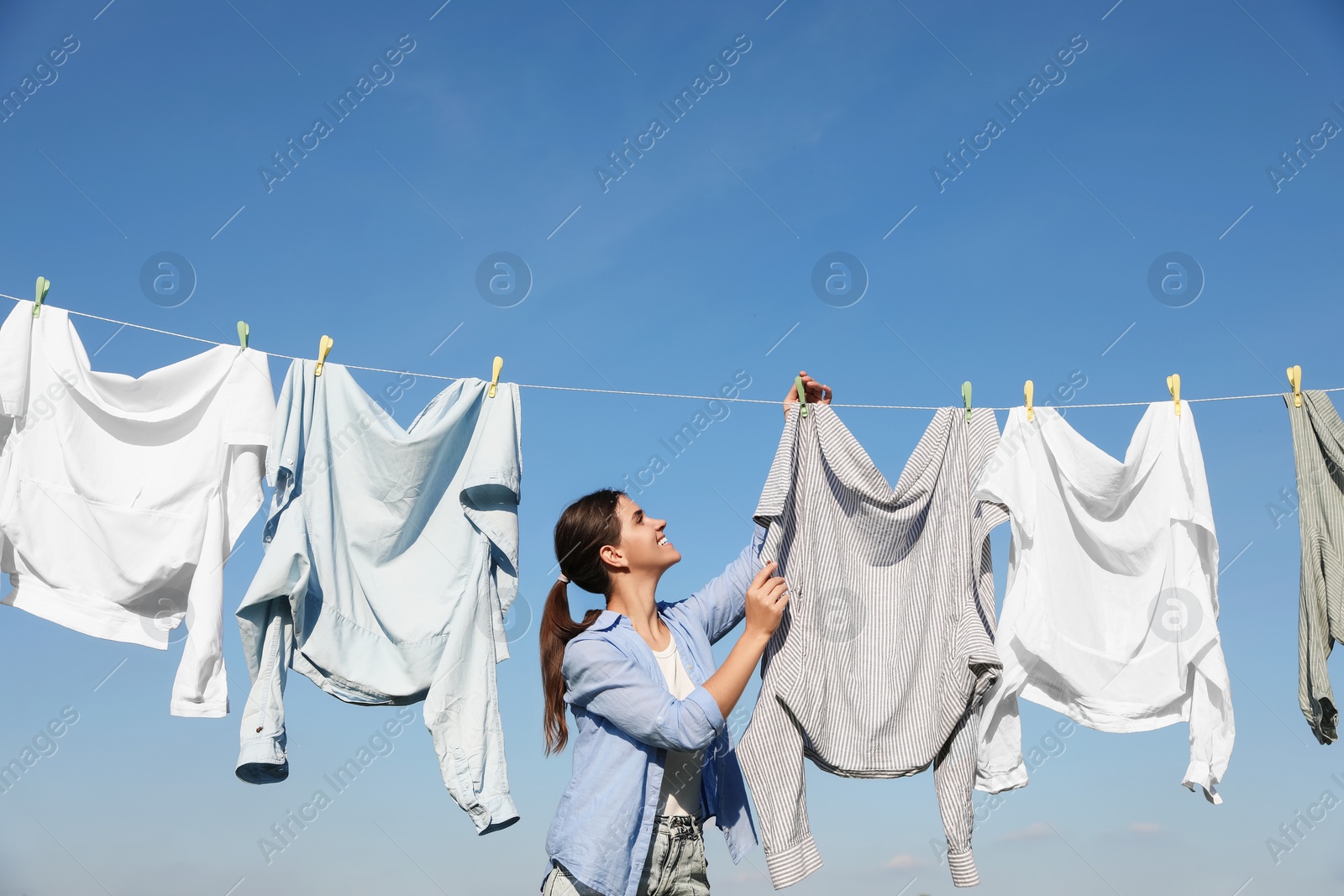 Photo of Woman hanging clothes with clothespins on washing line for drying against blue sky