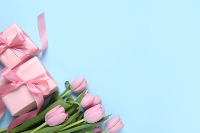 Photo of Beautiful gift boxes and pink tulip flowers on light blue background, flat lay. Space for text