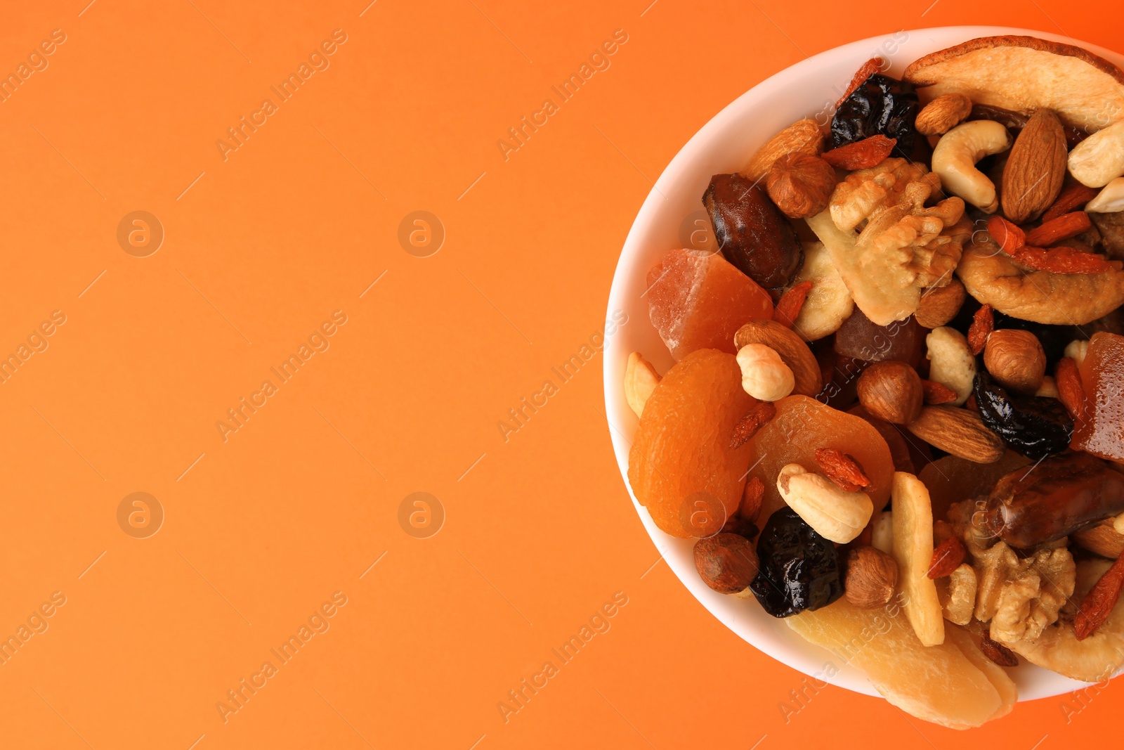 Photo of Bowl with mixed dried fruits and nuts on orange background, top view. Space for text