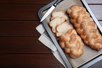 Photo of Baking tray with homemade braided bread on wooden table, top view and space for text. Traditional Shabbat challah