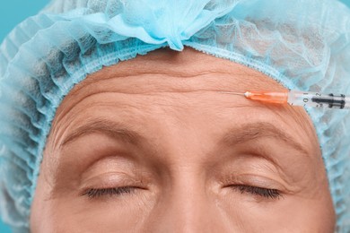 Senior woman getting facial injection on light blue background, closeup. Cosmetic surgery