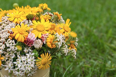 Photo of Pale yellow watering can with beautiful flowers on green grass, closeup. Space for text