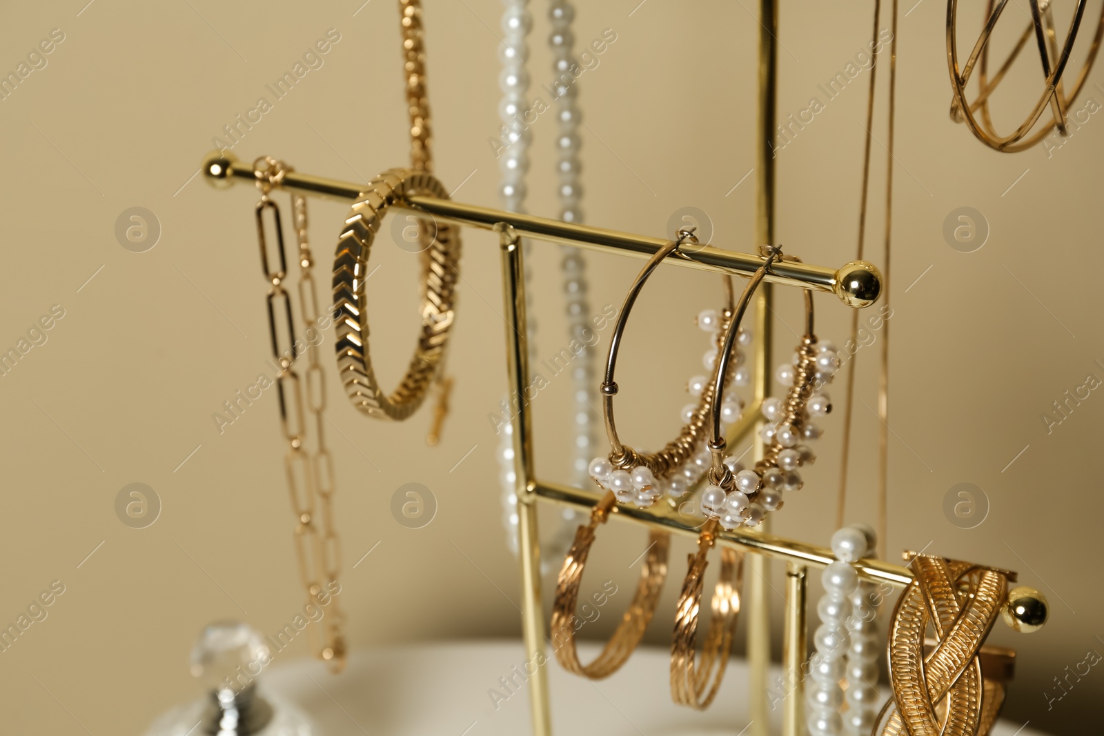 Photo of Holder with set of luxurious jewelry on beige background, closeup