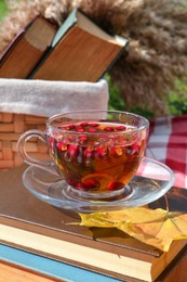 Photo of Cup of tea with hawthorn berries on books outdoors