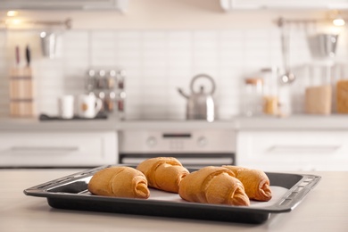 Photo of Baking tray with delicious croissants on kitchen table