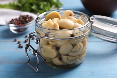 Photo of Delicious marinated mushrooms in glass jar on light blue wooden table