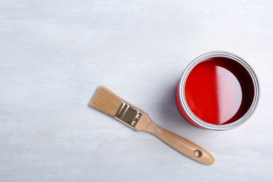 Photo of Can with red paint and brush on light background, top view. Space for text