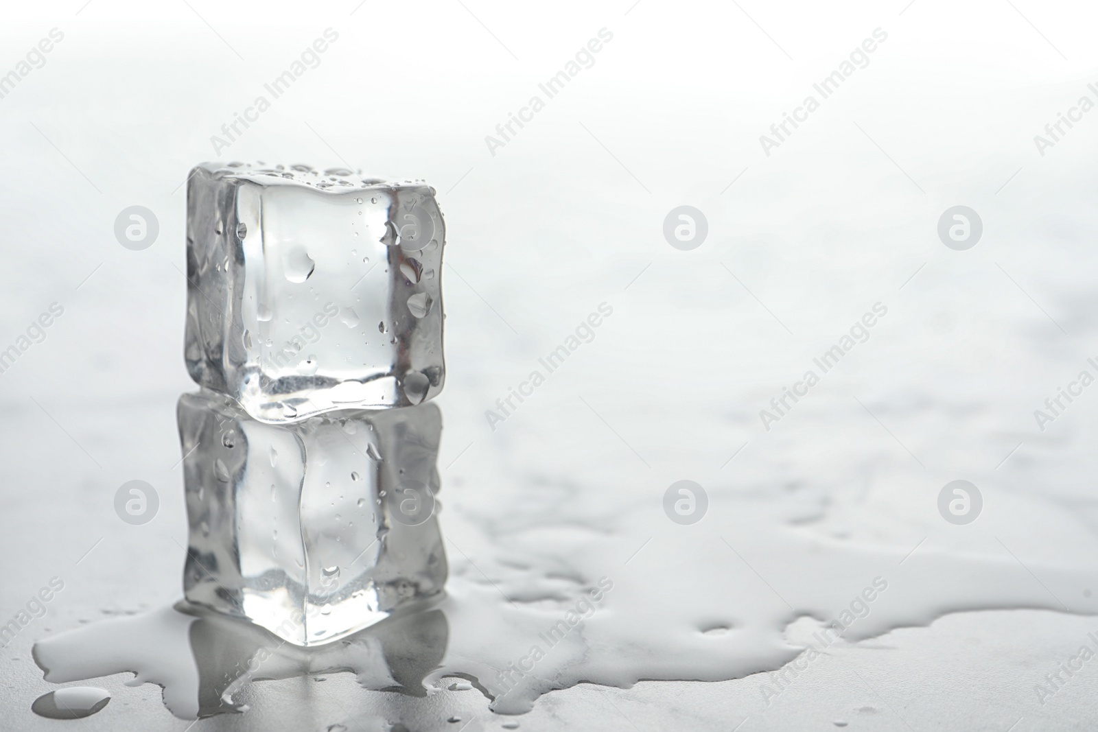 Photo of Wet ice cubes on white table, closeup. Space for text