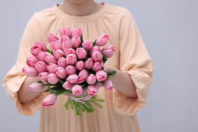 Photo of Woman holding bouquet of pink tulips on light grey background, closeup