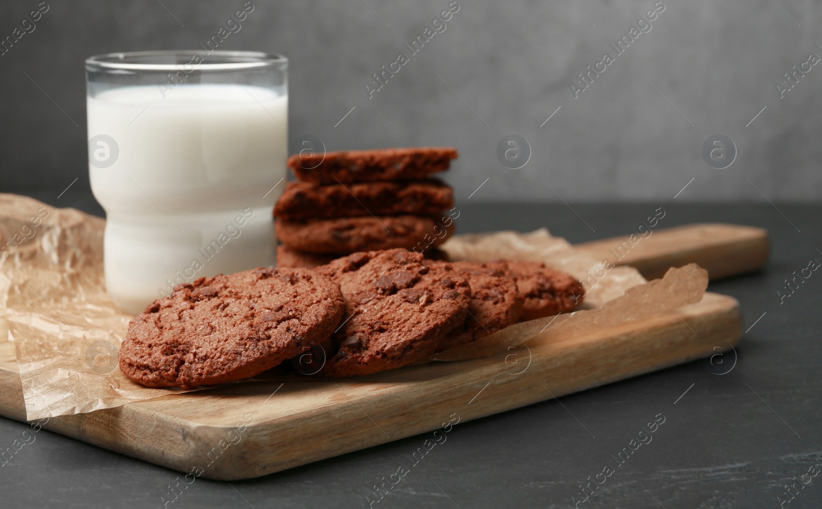 Photo of Board with tasty chocolate cookies and glass of milk on dark table. Space for text