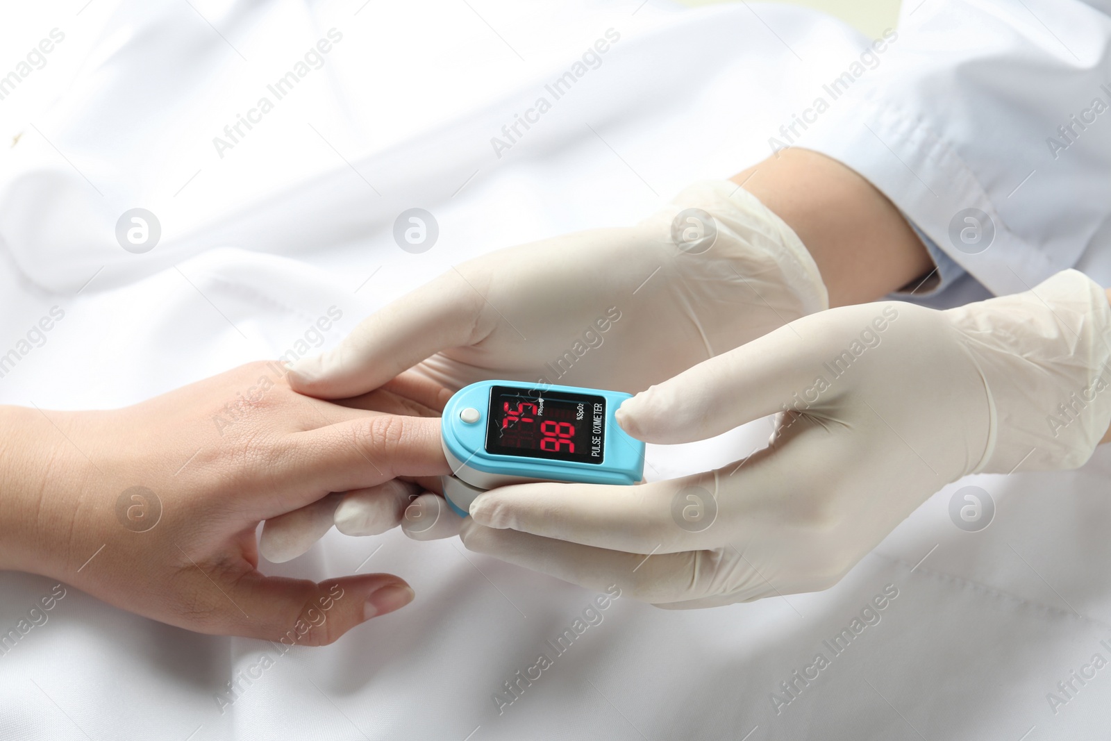 Photo of Doctor examining patient with fingertip pulse oximeter in bed, closeup