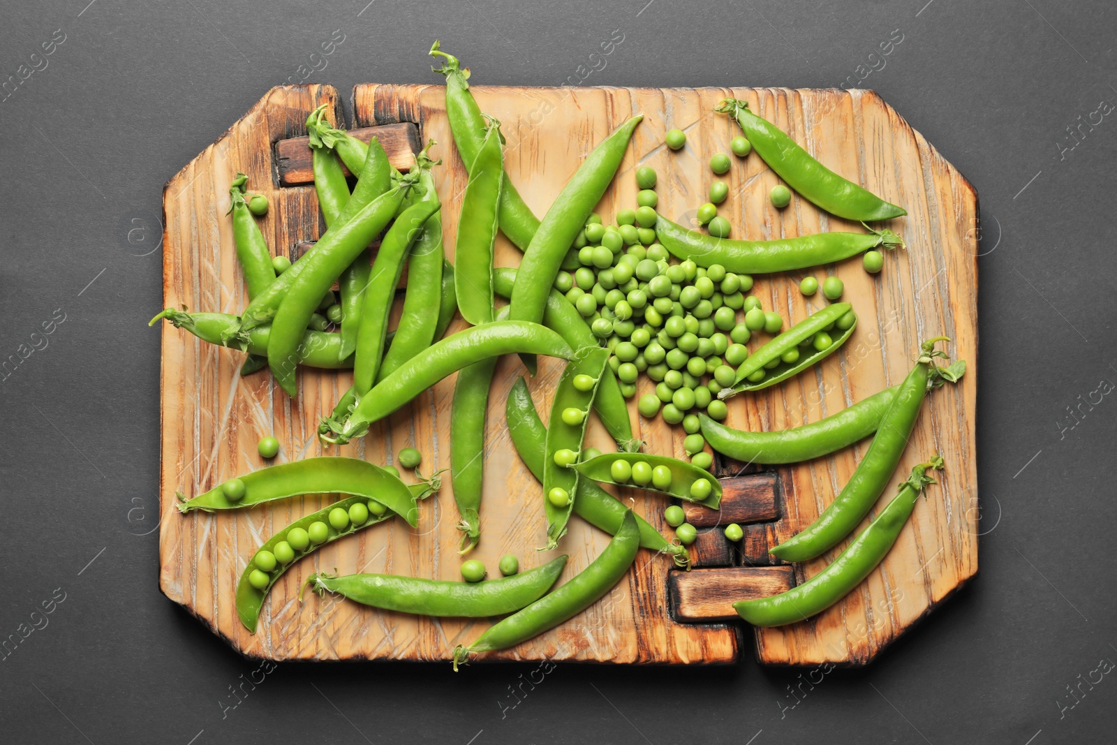 Photo of Wooden board with green peas on black background, top view