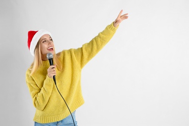 Photo of Emotional woman in Santa Claus hat singing with microphone on light grey background, space for text. Christmas music