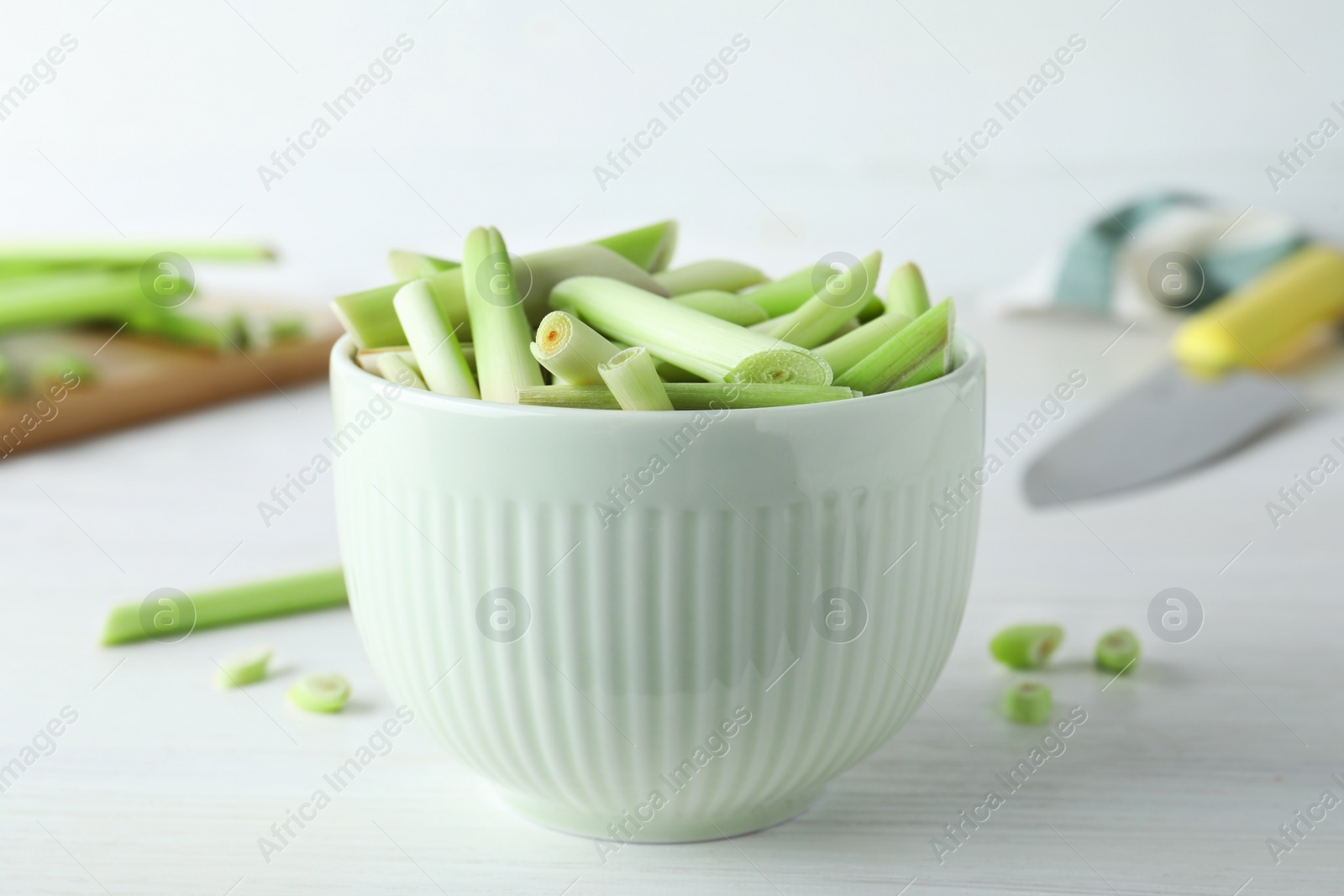 Photo of Bowl with fresh lemongrass stalks on white table, closeup