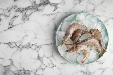 Raw shrimps with ice on marble table, top view. Space for text