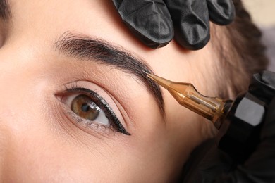 Photo of Young woman undergoing procedure of permanent eyebrow makeup in tattoo salon, closeup