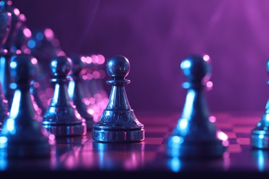 Photo of Chess pawn on checkerboard in color light, selective focus