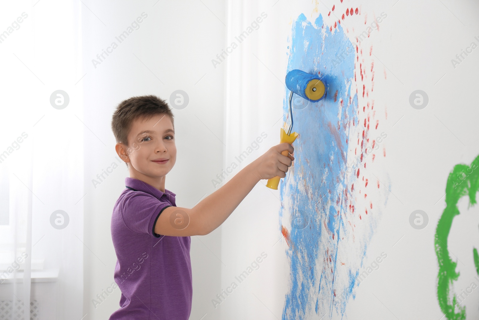 Photo of Little child painting wall with roller brush indoors