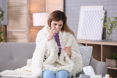 Photo of Sick woman with thermometer suffering from cold on sofa at home