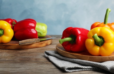 Boards with ripe bell peppers on wooden table against light blue background