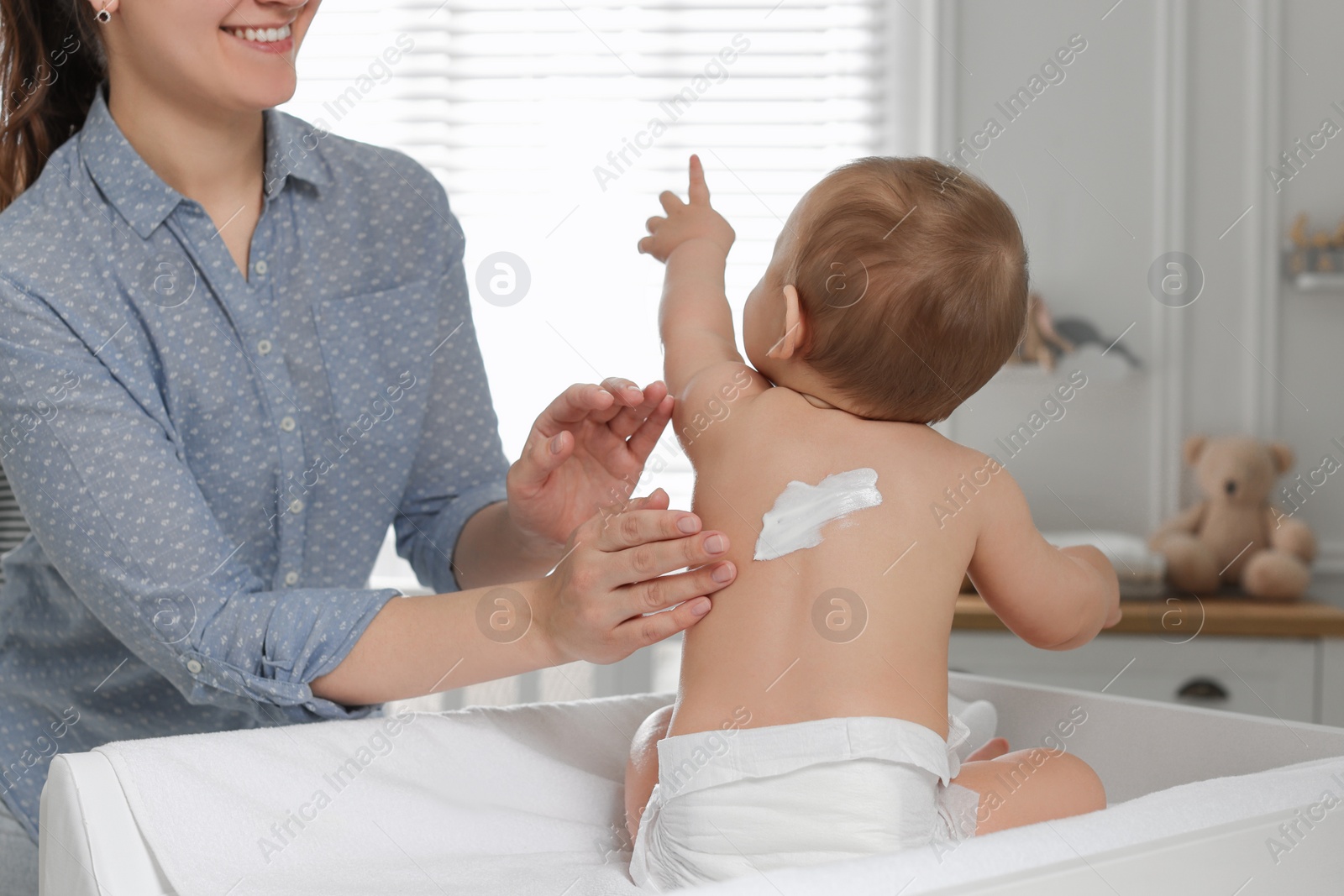 Photo of Mother applying body cream on her little baby at home, closeup