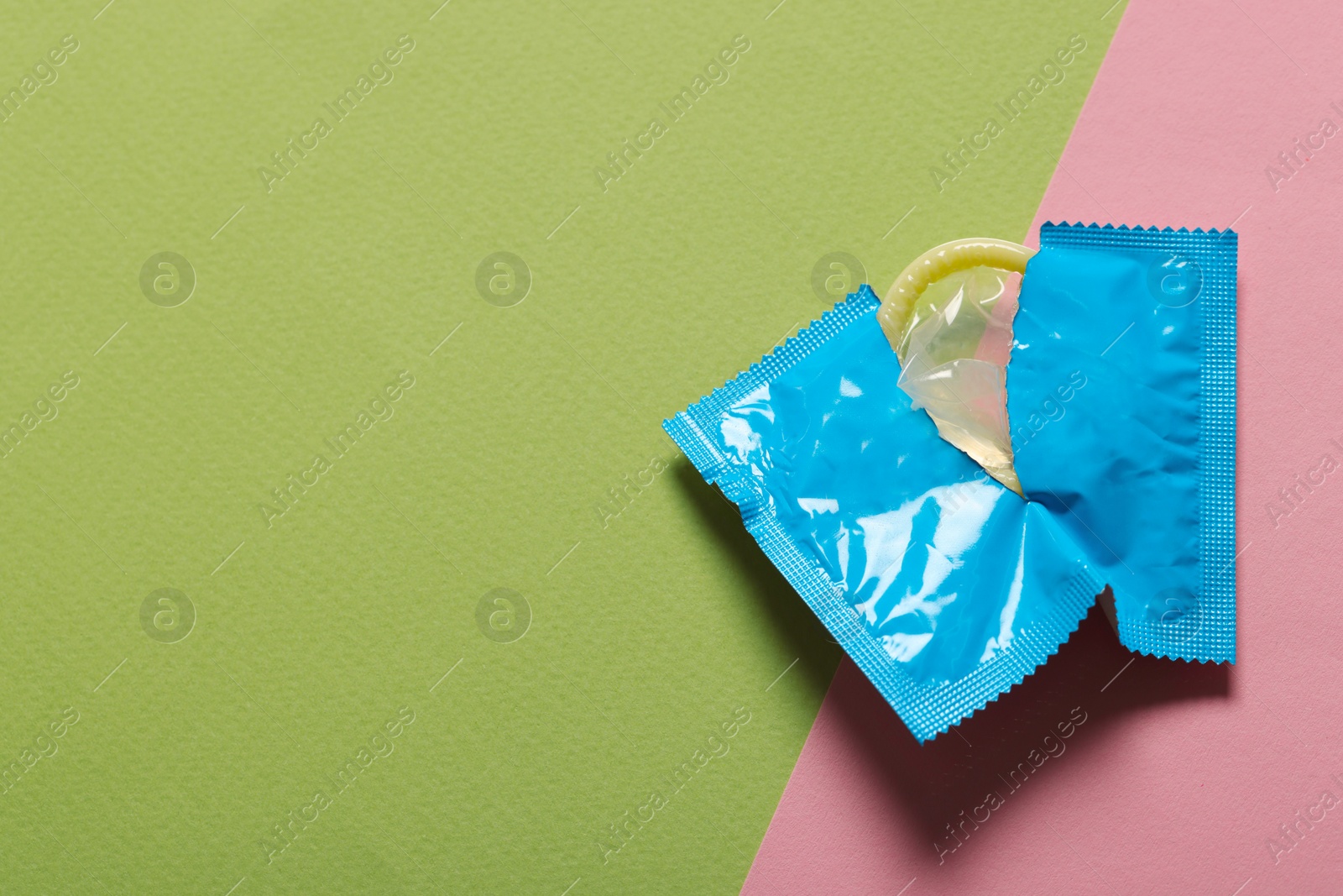 Photo of Condom in torn package on color background, top view with space for text. Safe sex