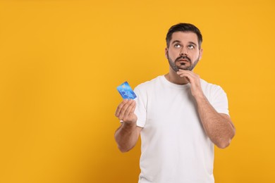 Confused man with credit card on orange background, space for text. Debt problem