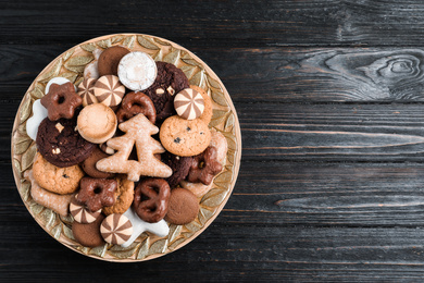 Delicious cookies in plate on black wooden table, top view. Space for text