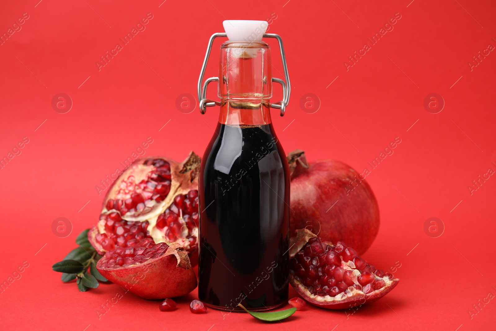 Photo of Tasty pomegranate sauce in bottle and fruits on red background, closeup