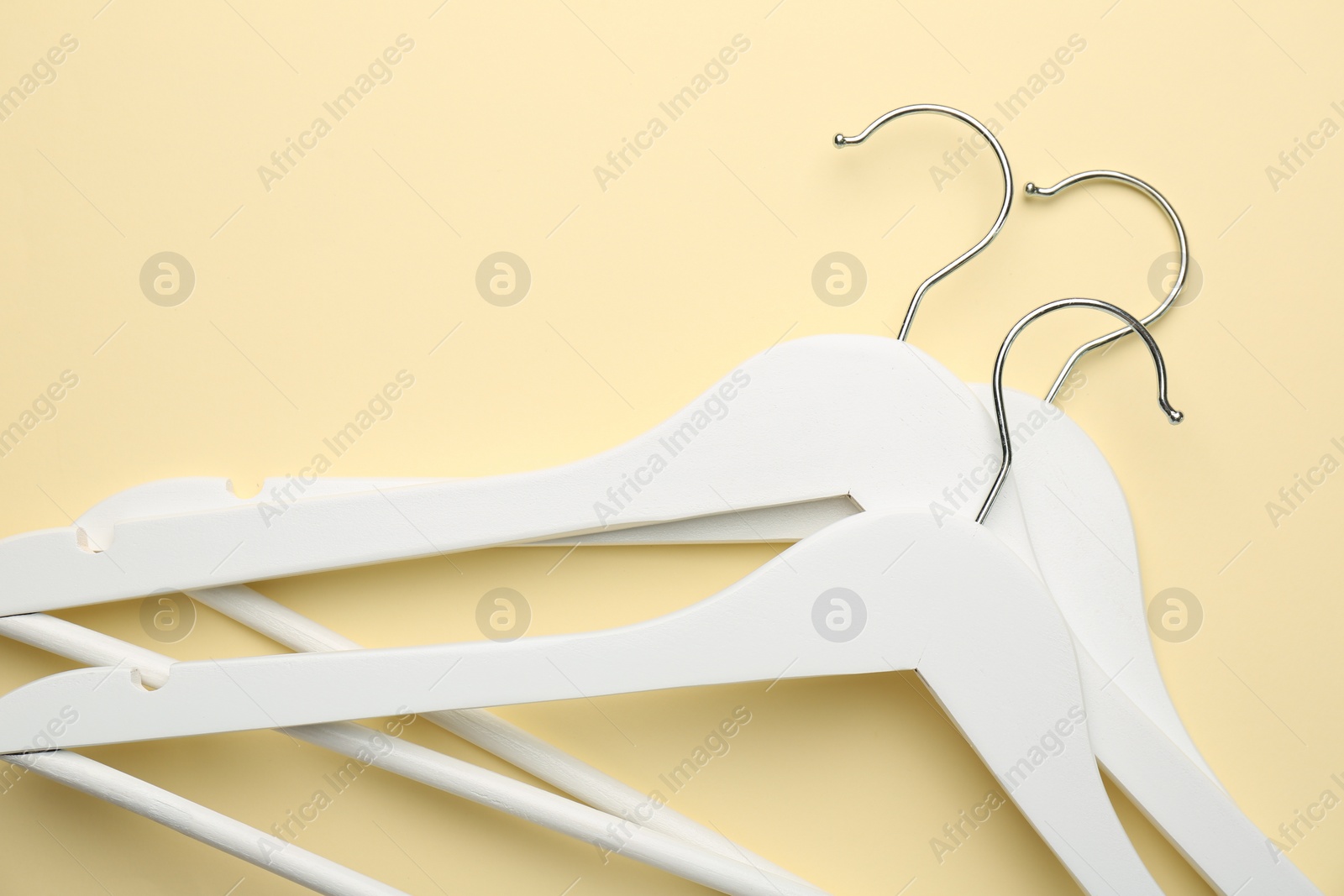 Photo of White hangers on pale yellow background, top view. Space for text