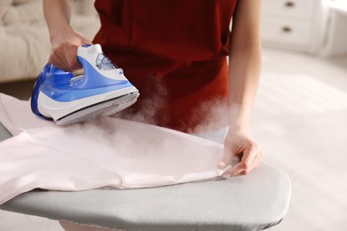 Photo of Woman ironing clean sweatshirt on board indoors, closeup