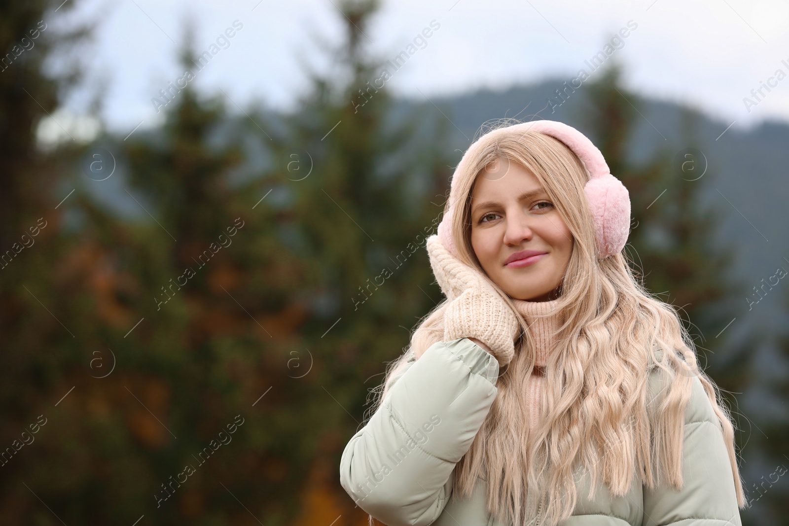 Photo of Young beautiful woman wearing warm earmuffs in mountains