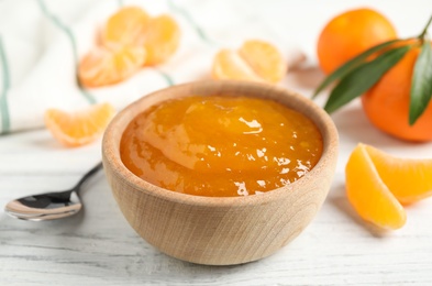 Photo of Tasty tangerine jam in wooden bowl on white table