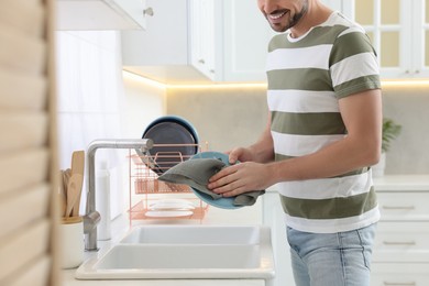 Man wiping plate with towel above sink in kitchen, closeup
