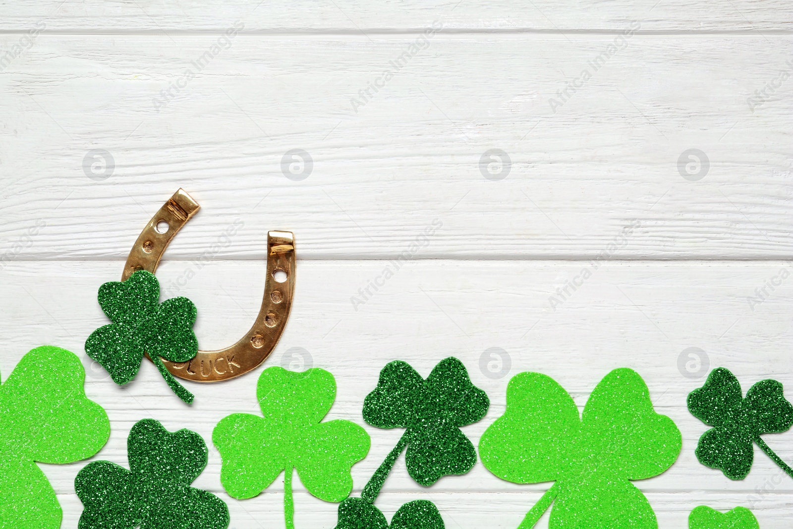 Photo of Flat lay composition with clover leaves and horseshoe on white wooden table, space for text. St. Patrick's Day celebration