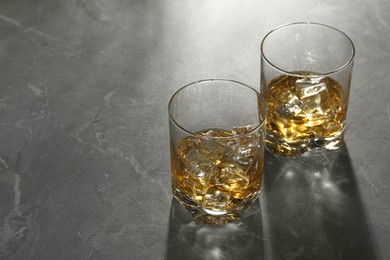 Whiskey with ice cubes in glasses on grey marble table, space for text