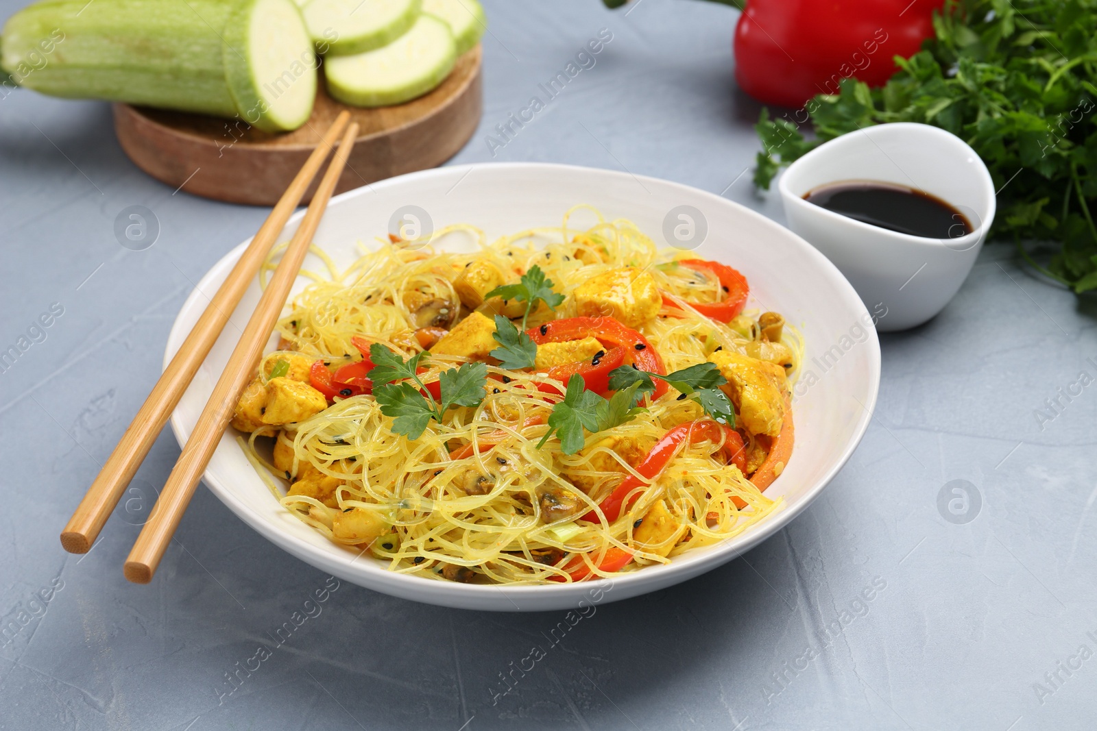 Photo of Stir-fry. Delicious cooked noodles with chicken and vegetables in bowl served on gray textured table