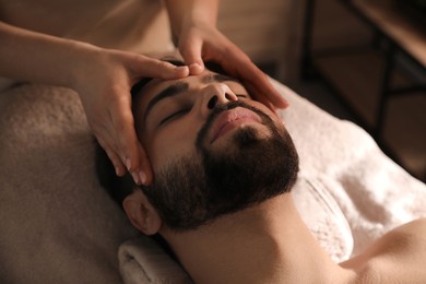 Photo of Young man receiving facial massage in beauty salon