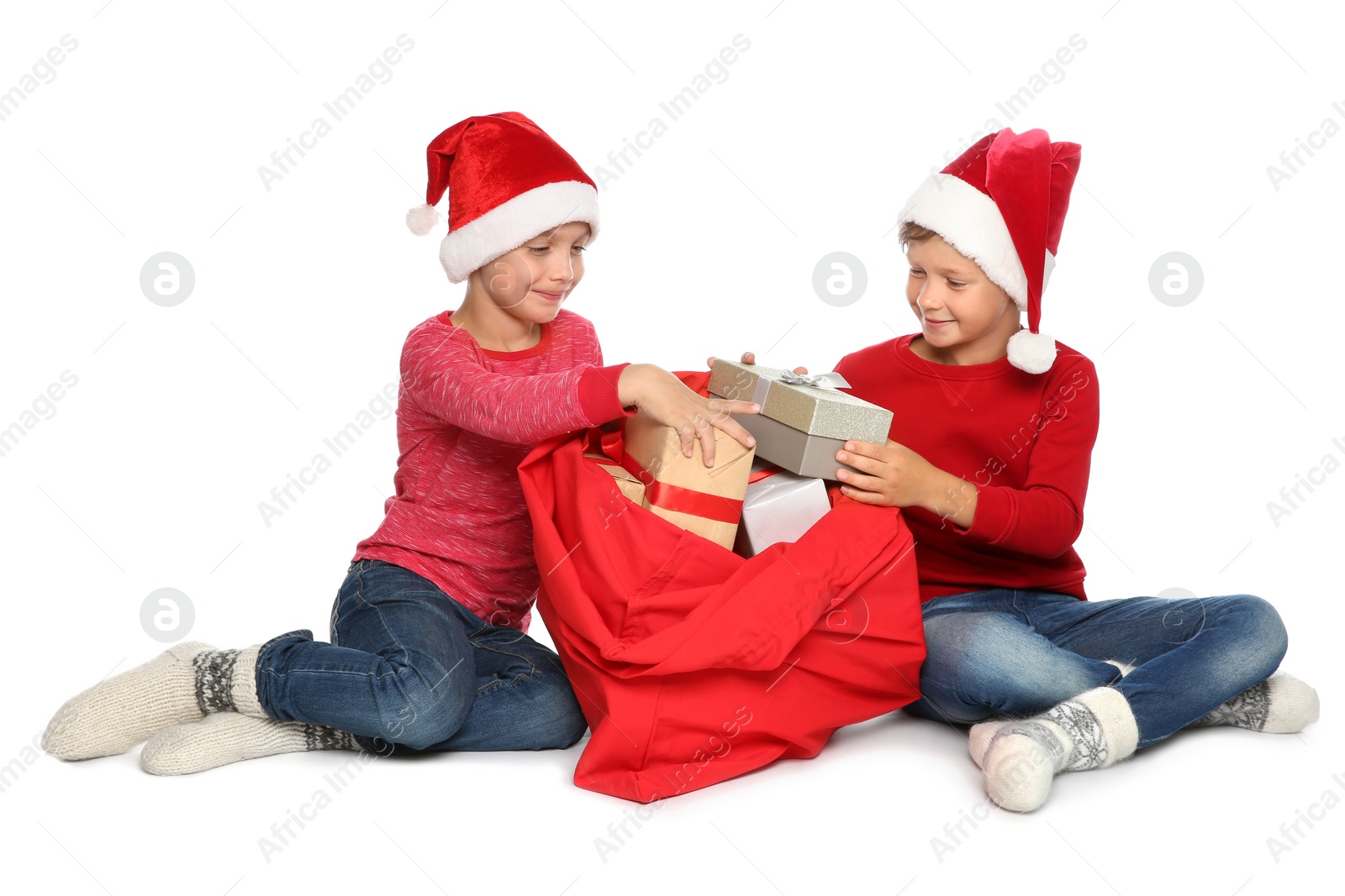 Photo of Cute little children in Santa hats pulling gift boxes out of red Christmas bag on white background