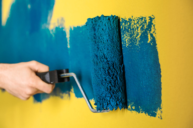 Photo of Man painting yellow wall with blue dye, closeup