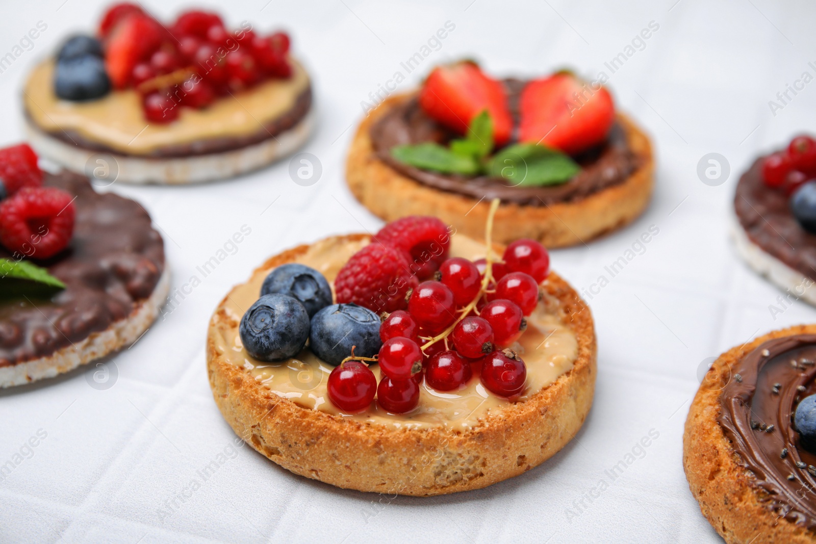 Photo of Fresh rice cakes and rusks with different toppings on white table, closeup