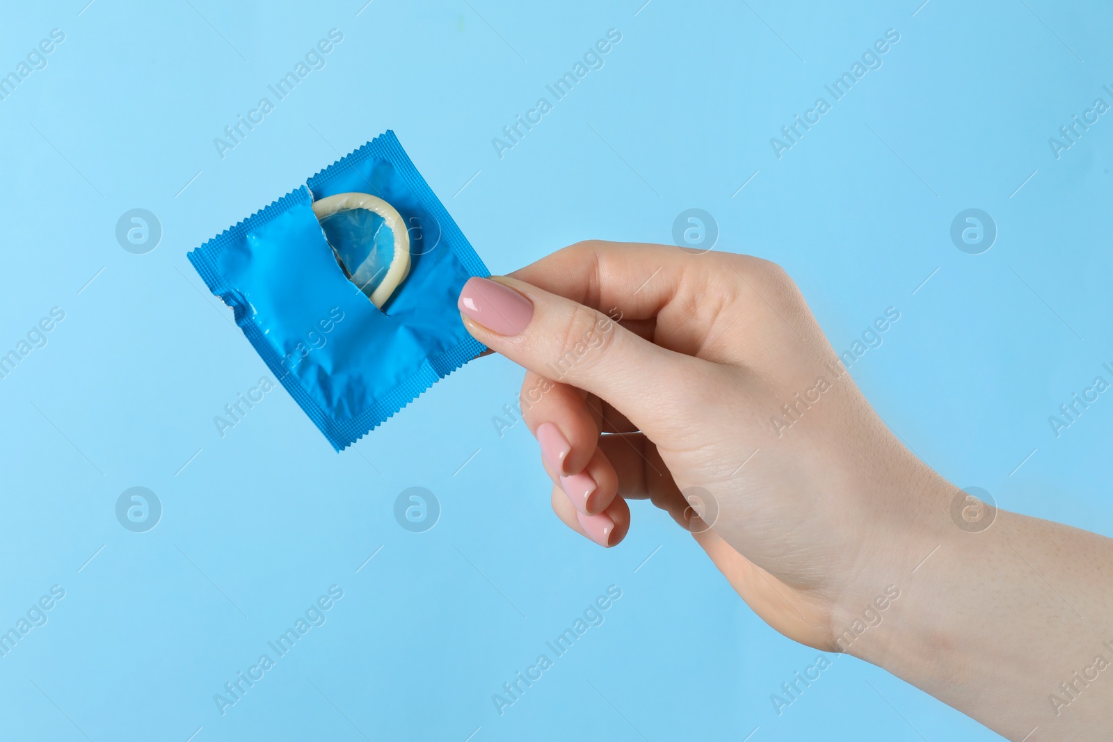Photo of Woman holding condom on light blue background, closeup