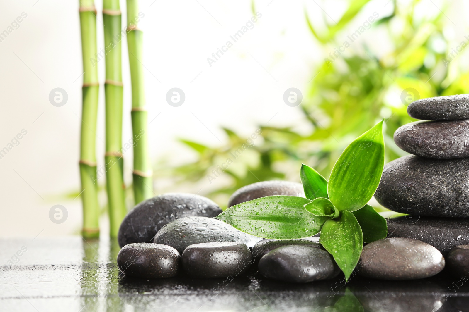 Photo of Bamboo leaves with spa stones on table against blurred background. Space for text