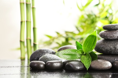 Photo of Bamboo leaves with spa stones on table against blurred background. Space for text