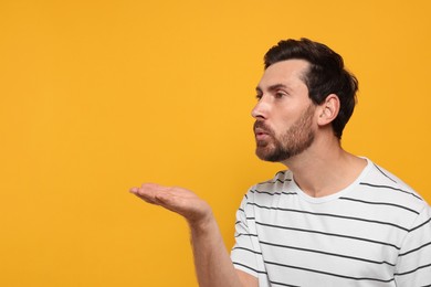 Handsome man blowing kiss on orange background. Space for text