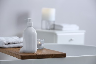 Photo of Bottle of bubble bath with foam, towel and candle on tub in bathroom, space for text