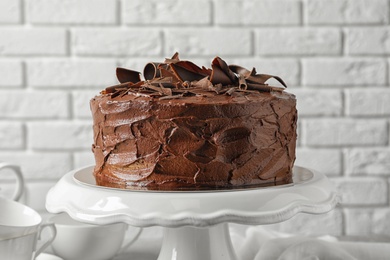 Stand with tasty homemade chocolate cake near white brick wall