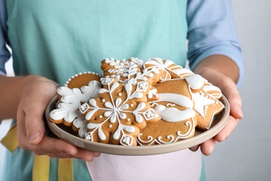 Photo of Woman with plate of delicious gingerbread Christmas cookies on grey background, closeup