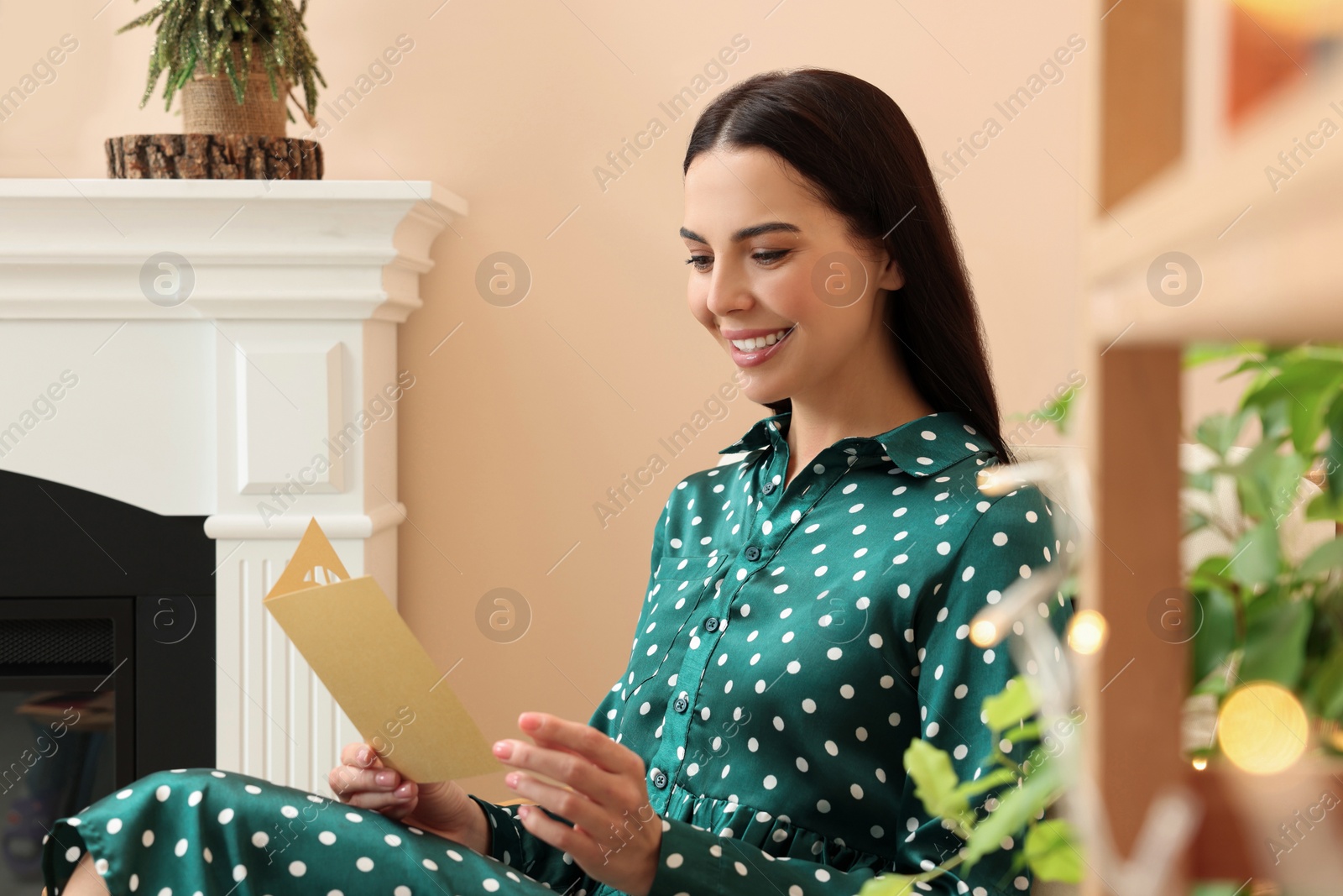 Photo of Happy woman reading Christmas greeting card in living room